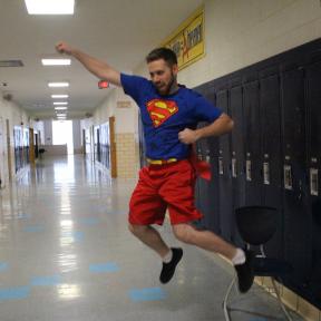 Teacher in superman costume jumping in the air like a clown.