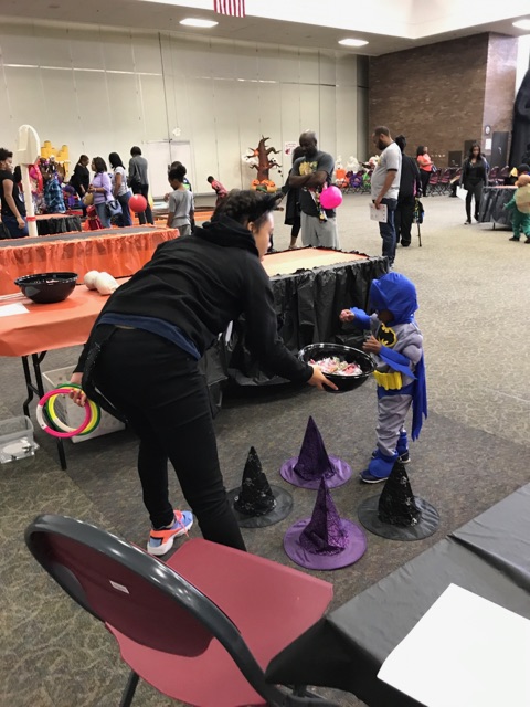 Female student sharing a bowl of candy with a small child in a costume