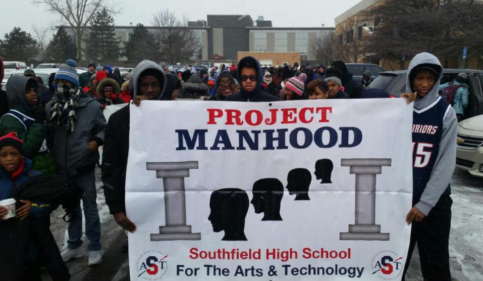 Young man at a parade holding a Project Manhood banner.
