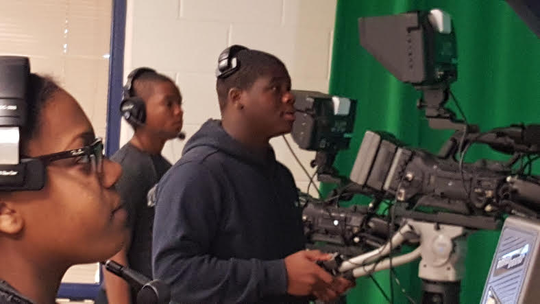 Three students using a TV camera wearing headphones